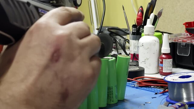 Worker cuts out batteries from custom pack with mini grinding tool in workshop closeup. Electrician hand cuts metal connector on power elements at workplace