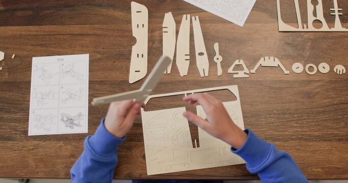 Little boy hands draw out airplane body plywood detail of sheet at desk closeup. Schoolboy prepares old aircraft model parts construction set at home upper view