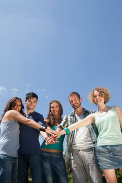 Group of people smiling outdoors showing unity with joined hands