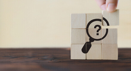 Hand placing wooden puzzle piece with magnifying glass and question mark on wooden blocks