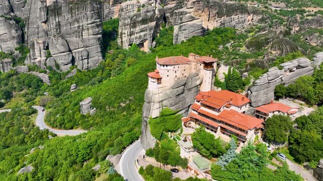 Aerial drone flight towards the Roussanou Monastery (St. Barbara) in Meteora, Greece. View of the convent built on a pillar, with winding roads and massive rock formations
