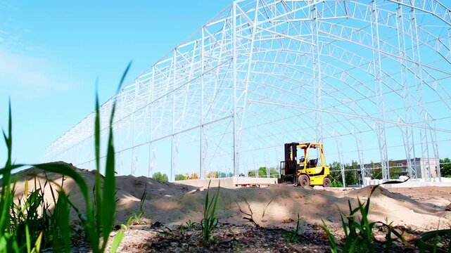 Green grass rises against blue sky with bright sunlight and open structural framing and forklift