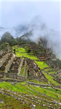 Morning sunrise Machu Picchu Inca trail tourist circuit terrances landscape sunny foggy clouds Peruvian Andes Peru Per&uacute; historic Inca Sanctuary Temple rainy season lush green jungle Vertical pan left