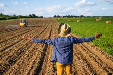 African farmer is standing in his agricultural field. He is supervising the spraying of the field.