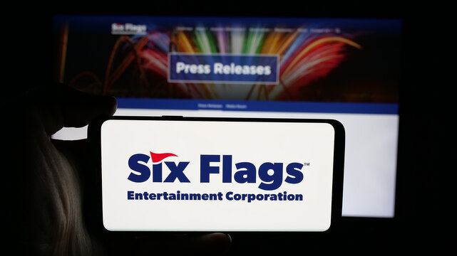Stuttgart, Germany - 12-19-2025: Person holding cellphone with logo of company Six Flags Entertainment Corporation on screen in front of webpage. Focus on phone display.