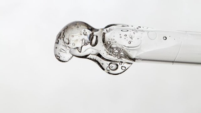 Slow movement of liquid transparent hyaluronic acid on a glass pipette macro, beauty background front view.