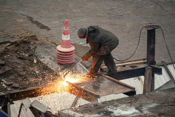 Construction worker cutting steel beam with gas torch during road maintenance and infrastructure repair, creating bright sparks at urban worksite
