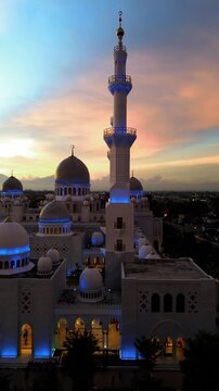 Aerial view of the Sheikh Zayed Grand Mosque in Surakarta, a replica of the Sheikh Zayed Grand Mosque in Abu Dhabi, UAE illuminated at sunset, featuring the large domes and tall shining minarets