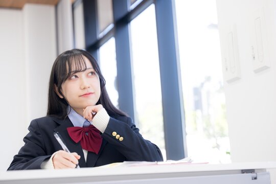 塾や学校、予備校などの教室で大学受験などの志望校の進路を悩む考える迷う、顎に手を当てる女の子　内申対策どうしようかな？