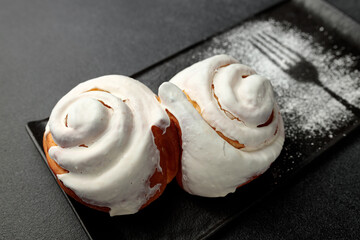 Fragrant cinnabons with cream on a black rectangular plate on a gray background