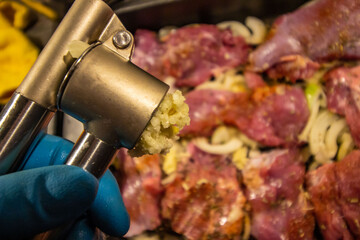 squeezing garlic onto meat sprinkled with seasonings and spices. close-up. cooking.