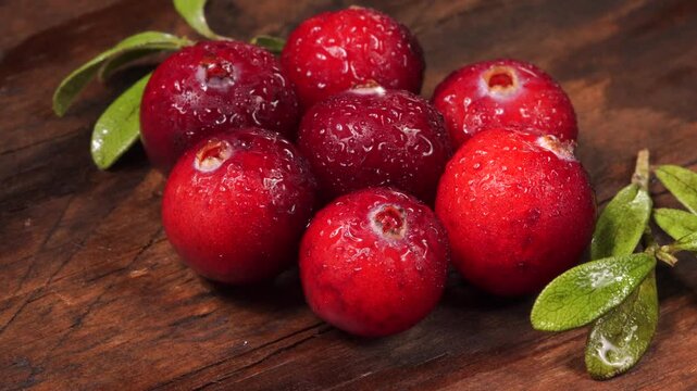 Cranberries on a wooden board. Simple pattern, leaves in the frame. Clean, washed berries in drops of water. Slow rotation.