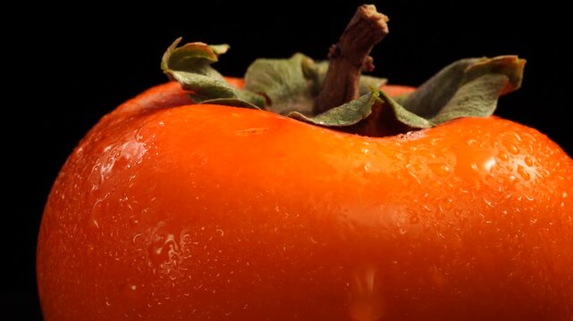 A persimmon rotates against a dark background. Water droplets. Close-up. Depth of field control.