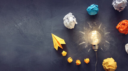 Lightbulb with crumpled paper and origami plane in creative idea concept on dark background with warm lighting for business inspiration