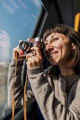 A beautiful, happy young woman takes a photo with a vintage analog camera from a train window. Concept of travel and discovery.
