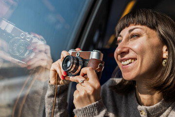 A beautiful, happy young woman takes a photo with a vintage analog camera from a train window. Concept of travel and discovery.