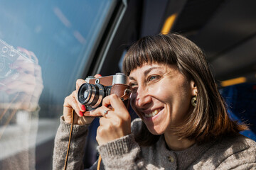 A beautiful, happy young woman takes a photo with a vintage analog camera from a train window. Concept of travel and discovery.