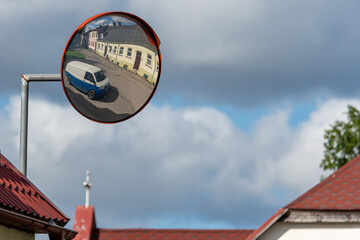 View of a round traffic mirror reflecting a street scene with a parked car and buildings.