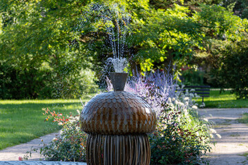Water fountain features a creative design with splashing water, surrounded by lush greenery.