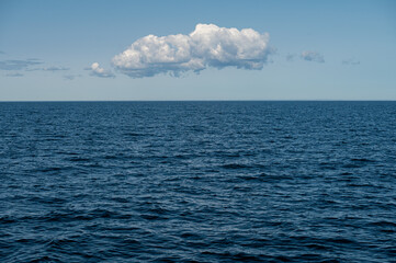 Blue ocean under a clear sky with a single cloud drifting calmly overhead