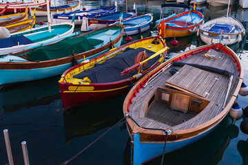 Obraz premium Traditional colorful wooden fishing boats moored in a calm Mediterranean harbor at sunset, vibrant nautical scene with reflections on dark water