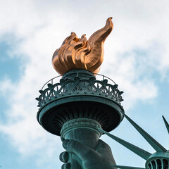 Statue of Liberty torch with flame against cloudy sky background  