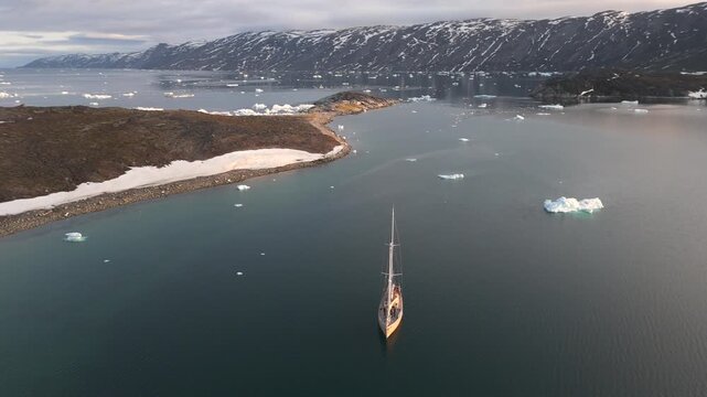 Yellow sailboat rests motionless in Greenland Arctic waters with small icebergs nearby
