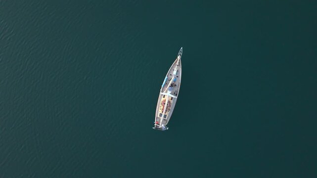 Top down aerial view shows sailboat rotating slowly on calm green sea