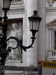 Elegant stone sculpture surrounded by ornate black lampposts in front of a Roman architectural backdrop.