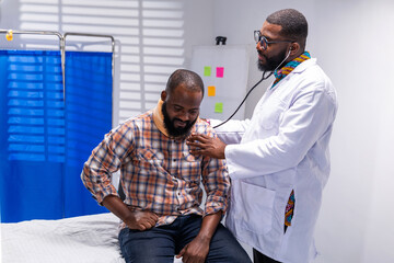 African doctor examines male patient wearing neck brace with stethoscope in hospital consultation room