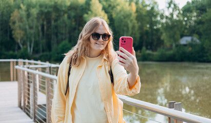 Happy woman chatting on phone outdoors. people concept. Smiling 30s blonde woman text messaging on smart phone at sunny day in the park, summer time.