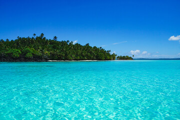 Fototapeta premium View of a lush palm-covered tropical island surrounded by crystal clear turquoise water in Aitutaki Lagoon, Cook Islands. Exotic island landscape, peaceful nature and paradise travel destination.