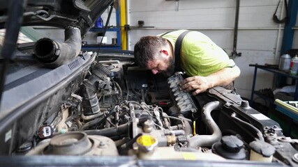 Professional repairman inspecting car engine at service. Adult auto mechanic working under hood of vehicle at garage. Male repairer checking automobile motor at workshop. Transport maintenance
