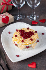 Festive puff salad with rice, chicken, eggs and cheese, garnished with pomegranate in heart-shaped plate for Valentines Day