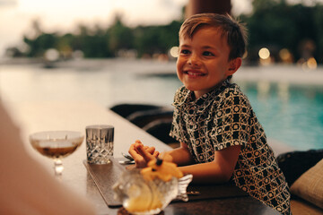 Smiling boy enjoying an outdoor dining experience at a poolside restaurant