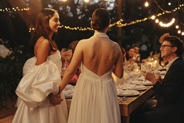 Two brides celebrating hand in hand at outdoor LGBTQ wedding reception