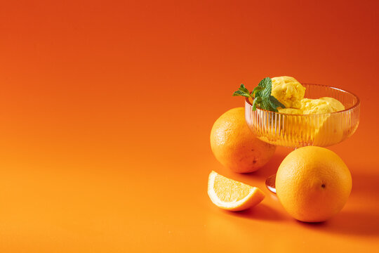 Orange sorbet in a glass bowl, arranged on a vibrant orange background with copy space.