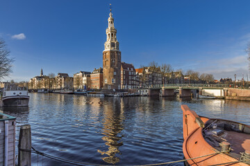 The historic Montelbaanstoren tower standing on the Oudeschans canal in Amsterdam, reflecting in the water on a sunny day with a bridge. Amsterdam Netherlands, 28 december 2025