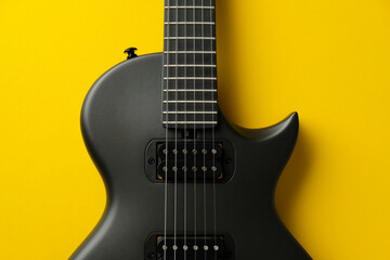 Symmetrical close-up of a black electric guitar body on a yellow background