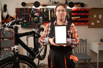 Mechanic woman doing bike servicing showing white screen on tablet. online replacement bicycle parts