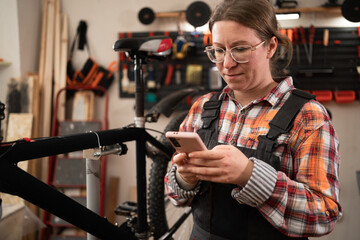 Young bicycle mechanic using a smartphone repairing bicycle in garage or workshop