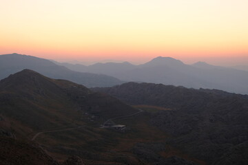 Fototapeta premium majestic mountain landscape at dawn with a winding road on a rugged slope under a vibrant orange and yellow sky