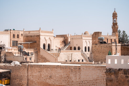 view of the historical stone architecture in the old town of Midyat Mardin Turkey featuring a church bell tower and traditional houses under a clear blue sky