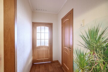 Fototapeta premium A narrow hallway with light wooden doors (one with frosted glass panels), wooden flooring, beige walls, and a large botanical mural on the right wall. Ceiling spotlights provide illumination