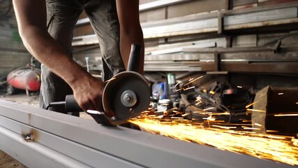 Male hands of young craftsman cuts iron using electric grind wheel at workshop. Arms of professional repairman sawing metal construction with a circular saw at garage or workplace. Slow motion