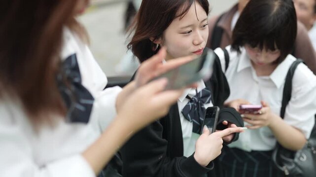 A group of girls are looking at their cell phones. One girl is holding a pink key chain