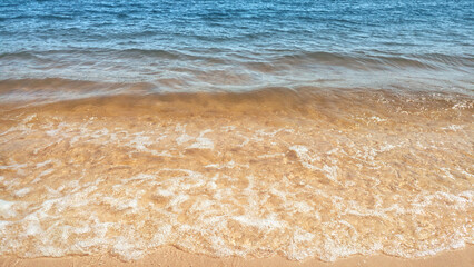The lake water waves with foam on the yellow sand beach. The summer mood backdrop.