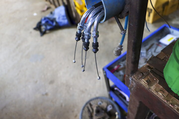 Closeup shot looking down at shiny metallic motorcycle cable hanging from mechanic stand in busy...