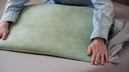 Human hands demonstrate a green pillow with dirty yellow stains sweat or saliva in a living room. Conscious home care and sustainable living concept. top view