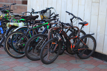 A collection of parked bicycles in various colors and styles. The scene shows a mix of mountain and city bikes on a paved surface.
